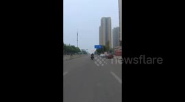 China: A Rider Puts on a Jacket While Driving.