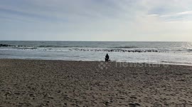 A woman sitting on a chair on an empty beach looks out to sea as her dog wanders around her on a sunny October day in Rome.