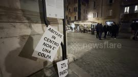A sign with the slogan 'living in the center is not a fault' and in the background a place with tables outside during the protest against the unlivability of some areas of the historic center, due to mass tourism, in Rome.