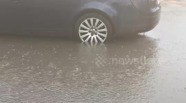 A car wheel sinks into the water accumulated in a parking lot and pedestrians are forced to jump to get through on a rainy day in February in a suburban area of ​​Rome.