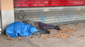 Two homeless men sleep on the floor in front of a closed shop shutter on a cold December day in a suburban area of ​​Rome.