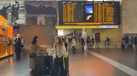 A woman with many large trolleys waiting while the incoming train board shows heavy delays of up to more than 3 hours at Termini Station in Rome.