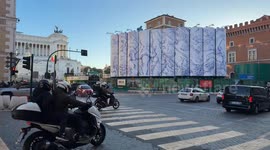 Vehicular traffic, pedestrians and police motorcycles escorting two buses to Piazza Venezia and in the background the construction site for the new Metro C stop and the Altar of the Fatherland in Rome.