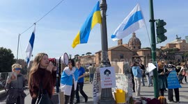 A protester speaks into a megaphone while Russian and Ukrainian flags are waving and a sign with the slogan 'Stop Putin's regime' hangs from a pole during the sit-in to demonstrate against the “Putin regime” and to promote the “Energy For Life” campaign b