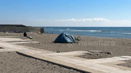 A homeless person's tent set up on the beach and the sea in the background with calm sea and clear sky at Lido di Ostia in Rome.