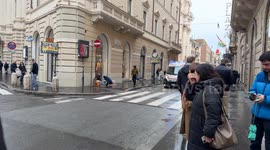 An ambulance with sirens blaring leaves Via del Corso at high speed on a gloomy day in Rome.