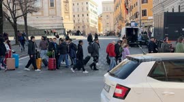 People and young tourists with their trolleys cross an intersection among the cars flowing in a central area of ​​Rome.
