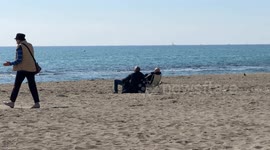 Two men sitting on deck chairs are sunbathing fully clothed on the beach of Lido di Ostia on a warm day in early March in Rome.