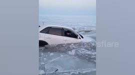 Motorist tries to scoop out water from sinking car after crashing into frozen lake
