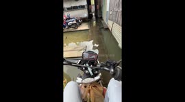 Motorcycle rider navigates narrow path through flooded homes