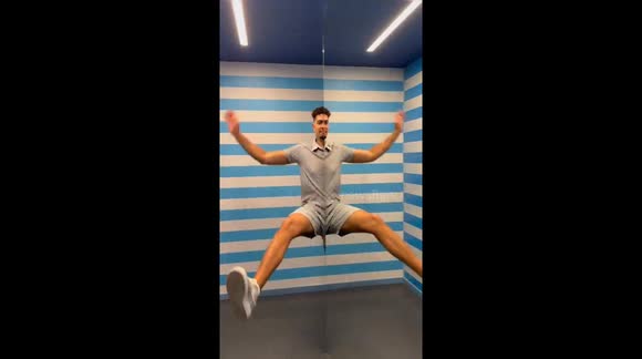 Young man shaking his body face to a distorting mirror to create a funny visual effect. Museum of Illusions of Malta, Island of Malta. 24 May 2025.