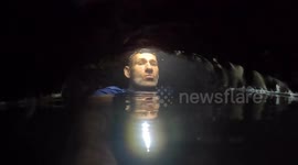 Caver squeezes past low airspace section in remote river cave