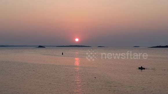 The sun rising behind Bakers Island and reflecting off Salem Sound while a rowboat passes