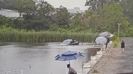 Car crashes into fish pond during a turn; driver escapes — nearby man calmly continues fishing throughout.