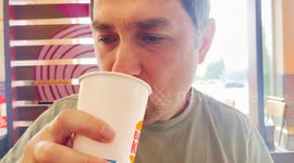 Close-up of a man drinking from a Burger King cup. He appears relaxed and thoughtful, enjoying a refreshing beverage inside a bright, modern restaurant setting