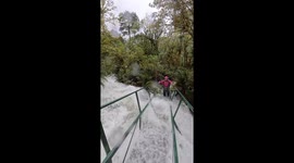 Hikers cross bridge by battling through knee-deep raging floodwater in terrifying footage