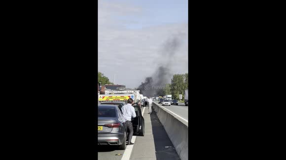 Thick black smoke rises from car fire on the M1 near Milton Keynes, as drivers step out of vehicles during major traffic standstill.