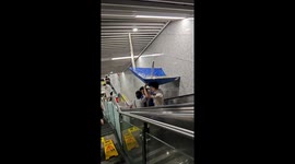 Subway staff hold makeshift umbrella to prevent leak from affecting escalator