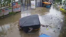 Auto-rickshaw carrying four tips over and begins sinking into rain-filled hole in road
