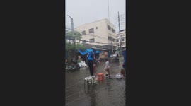 Children showering in the rain helps student cross flooded street using plastic chairs