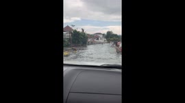 Driver maneuvers through flooded road as lake overflows after storm