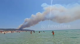 Beachgoers paddle as wildfire smoke looms in Spain