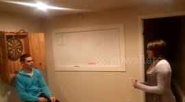 Man lets woman throw darts while he sits below board. Bad move!
