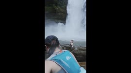 Hiker playing in waterfall screams as grasshopper clings to her back