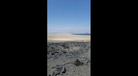 This is a first-person point-of-view (POV) video of a hike along a dirt trail in a rocky, arid landscape. The camera moves naturally, following the path as it descends a hillside. In the background, a stunning panoramic view is visible, featuring an expan