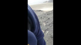 This first-person (POV) video immerses the viewer in a hike across a rocky, arid terrain. The camera alternates between shots of the ground, showing the hiker's feet, and panoramic views of a stunning coastal desert landscape. The most defining element is