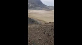 This vlogger/POV-style video captures the full experience of a hike in an arid, coastal landscape. It begins with sweeping panoramic views of rocky hills and a bay filled with hundreds of fishing boats under an overcast sky. The camera then turns to show 