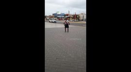 This found-footage video captures an impressive display of street football skill. A man, wearing a Peruvian national football team jersey, calmly walks across a busy public plaza while keeping a soccer ball in perfect balance on his head. Around him, urba