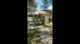 This POV-style video takes the viewer on a casual walk through a sunny university campus or public park. The camera moves across green areas and paved paths, capturing daily life: students or visitors walking, chatting, and relaxing on benches. An orange 