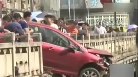 Passersby hold onto car hanging off bridge