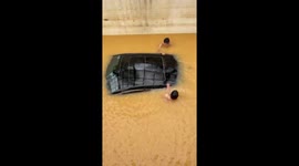 Two men try to rescue a car swept away in floodwaters