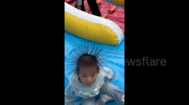 Hilarious moment toddler's hair stands on end after coasting down inflatable slide