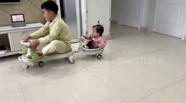 Adorable moment 1-year-old girl bobs head in delight while playing with older brother in wiggle car