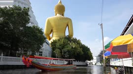 Tourists feed fish in front of giant Buddha statue in Bangkok
