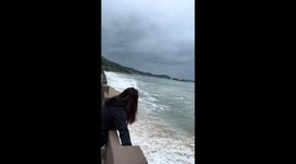Waves crash into tourist as she poses for pictures next to the sea
