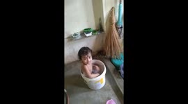 A one-year-old boy happily bathes in a bucket at home in India. Traditional Indian baby bathing.