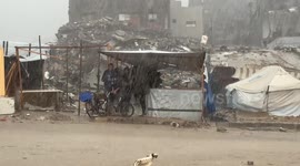 Gazan mother uses pot to scoop water out of flooded tent so children don't get sick
