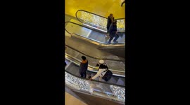 Guy wears cat like a parrot on his shoulder whilst riding down an escalator in shopping centre.