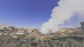 A hill of junk made of car parts, metal and wood is burning. Three water cannons shoot at the fire at 100 liters per second.