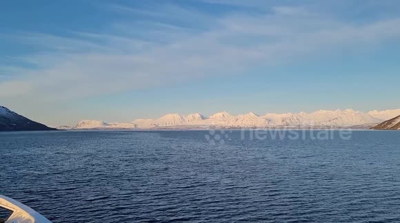 Raw footage from a boat travelling through the norwegian arctic cercle in April. Crystal-clear open Arctic waters (no floating ice), dramatic iced-covered mountain in thawing, and a clear sky. Authentic strong polar wind sound throughout.
