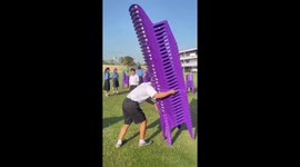 Schoolboy carries huge stack of chairs across field