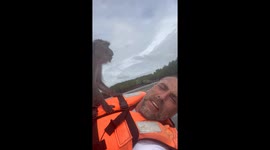 A tourist films a wild monkey standing on top of him while he lies on a kayak in the middle of a river in Koh Lanta, Thailand.