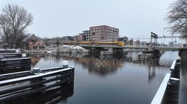 NS train travels along the railway through a Dutch winter landscape of snow-covered canals, houses.