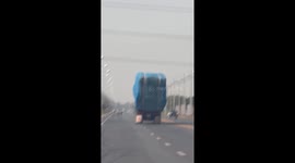 Truck overloaded with straw bales wobbles and topples over