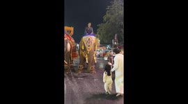 Grandmother helps toddler give money to elephants during a festival