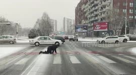 Pedestrian crawls over icy road crossing during snow in North Macedonia